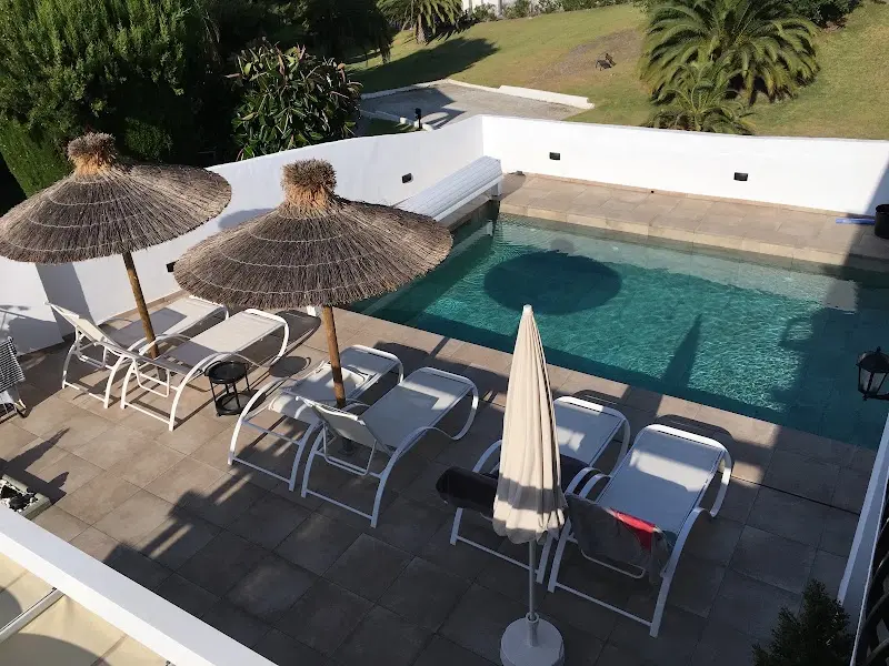 Piscina vista desde arriba con tumbonas blancas y sombrillas de brezo en el solárium