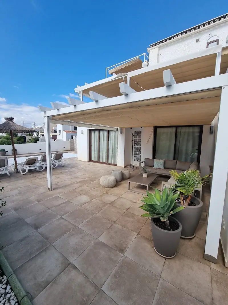 Porche con pérgola, sofá, mesa baja y plantas en macetas junto a la zona de piscina