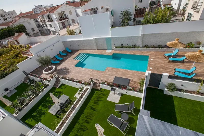 Piscina comunitaria con solárium de madera y hamacas, vista desde arriba sobre los jardines