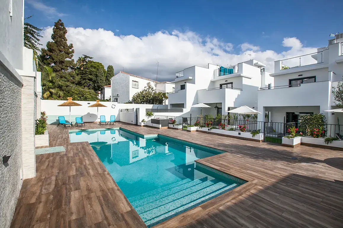Piscina comunitaria con solárium de madera y casas blancas alrededor en Casas de la Seda