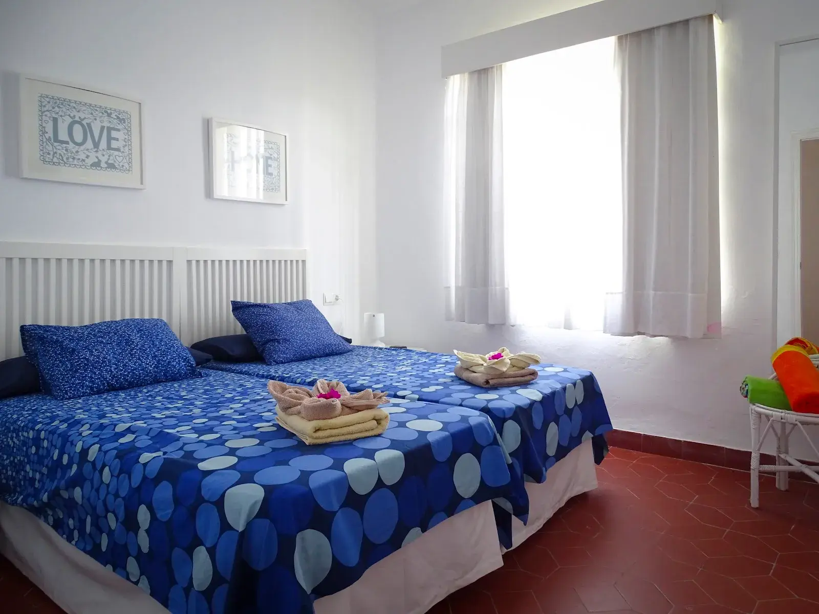 Dormitorio con dos camas de colcha azul de lunares y toallas preparadas