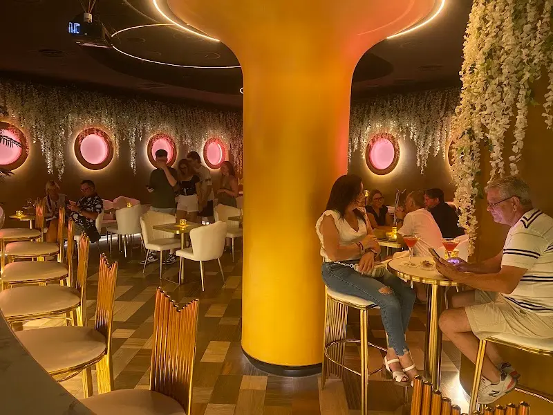 Clientes tomando cócteles en las mesas altas del bar, con una gran columna iluminada en naranja