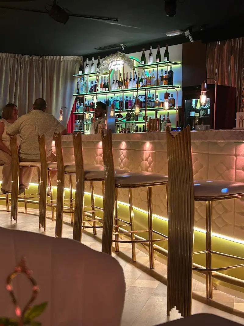 Barra con taburetes dorados y estanterías iluminadas llenas de botellas de champán y licores