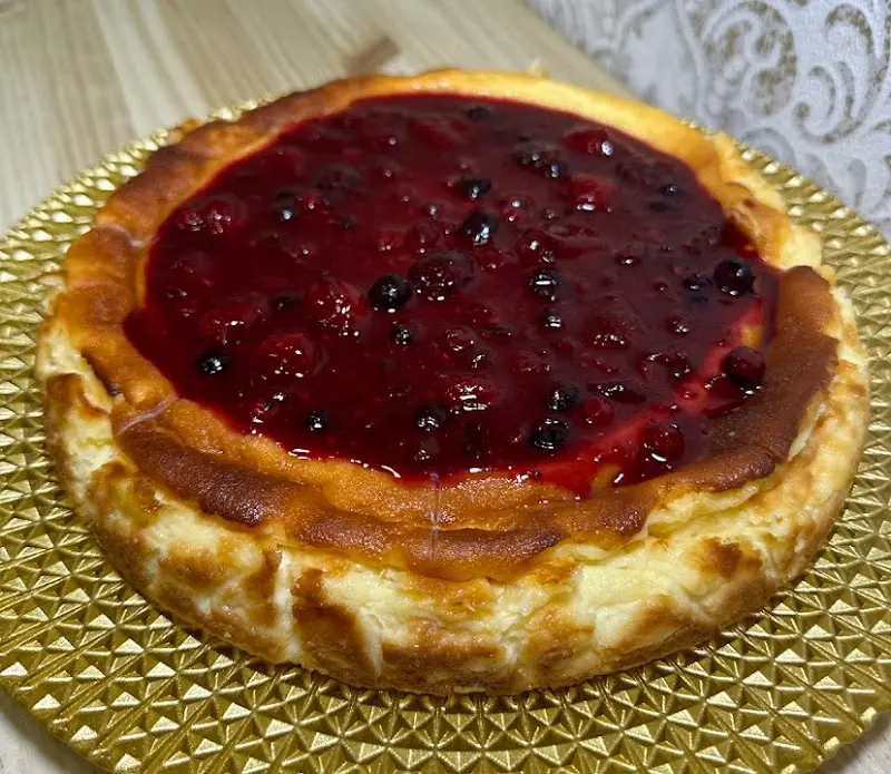 Tarta de queso entera con cobertura de frutos rojos sobre bandeja dorada