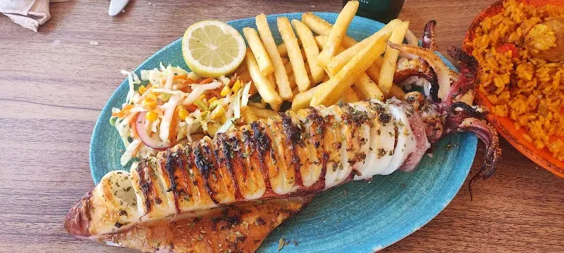 Calamar a la plancha con patatas fritas, ensalada y limón, junto a un plato de arroz