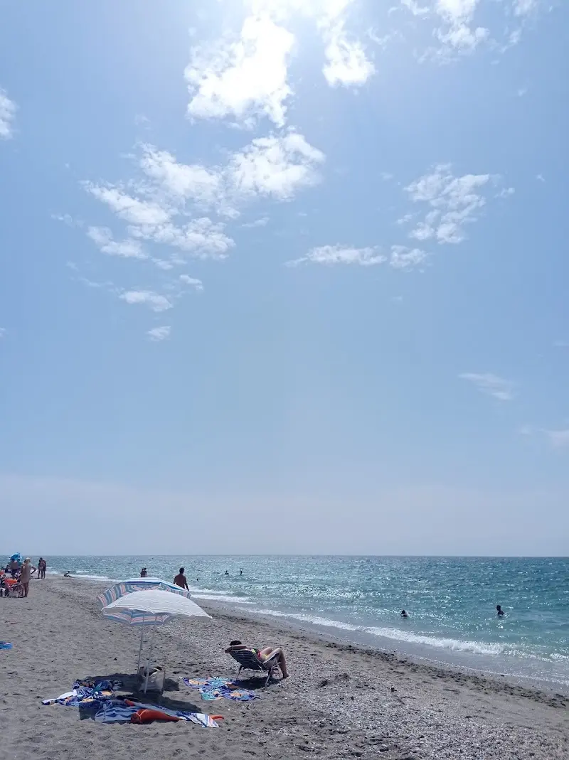 Bañistas y una sombrilla en la orilla de El Playazo en un día soleado