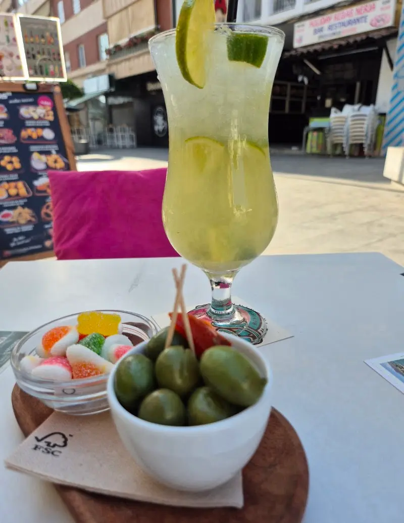 Cóctel con lima y hielo picado servido con aceitunas y gominolas en la terraza
