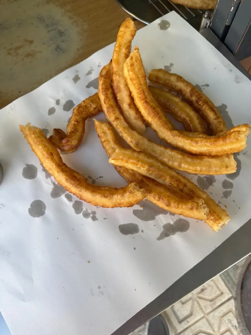 Porción de churros recién fritos sobre papel junto a la freidora