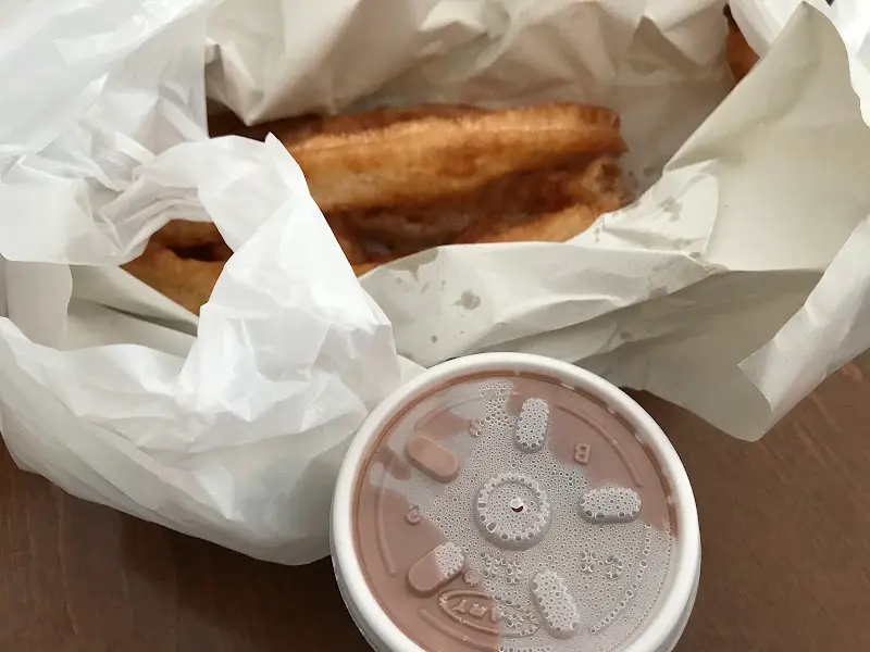 Churros para llevar envueltos en papel con un vaso de chocolate caliente