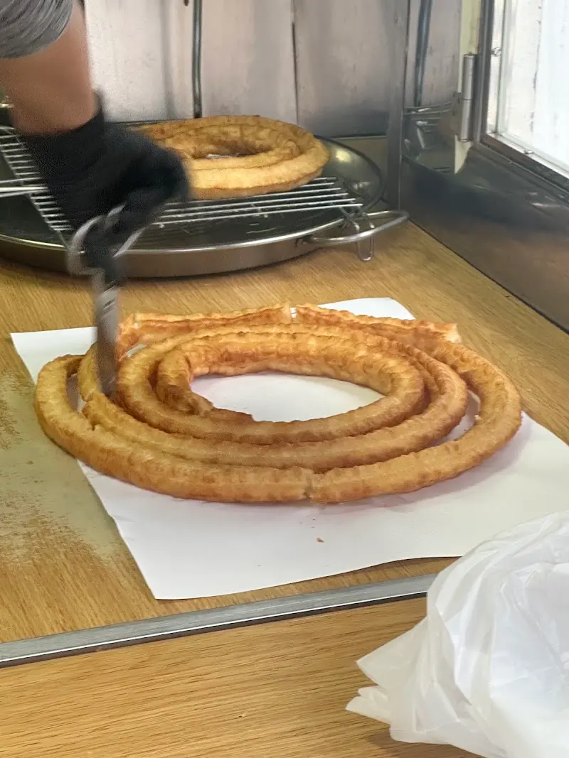Churrero cortando la rueda de churros con tijeras sobre el mostrador de madera
