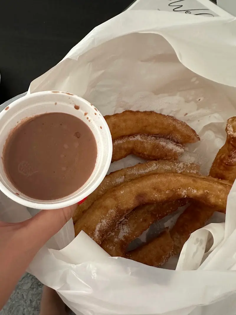 Churros con azúcar en una bolsa y un vaso de chocolate para mojar, de la churrería de Av. de Pescia