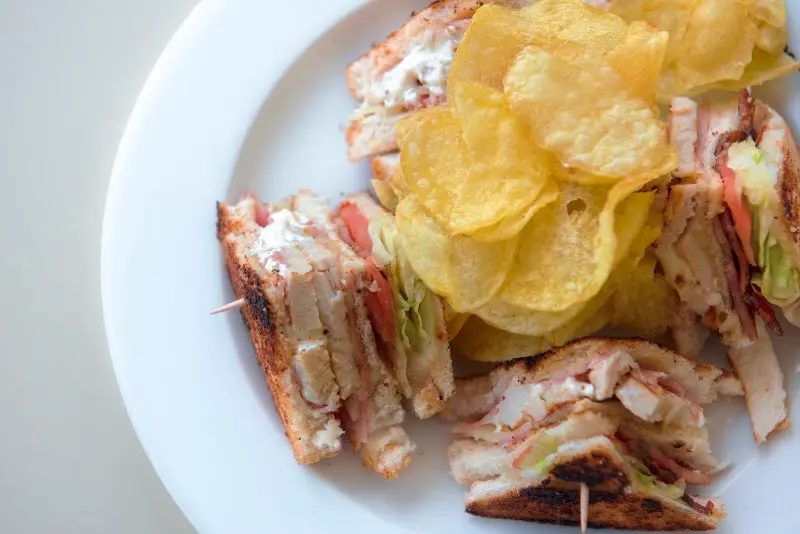 Sándwich club cortado en triángulos con patatas fritas en un plato blanco