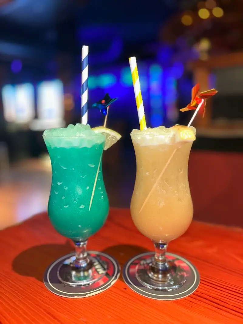 Dos cócteles tropicales, uno azul y otro cremoso, con pajitas de rayas y molinillos