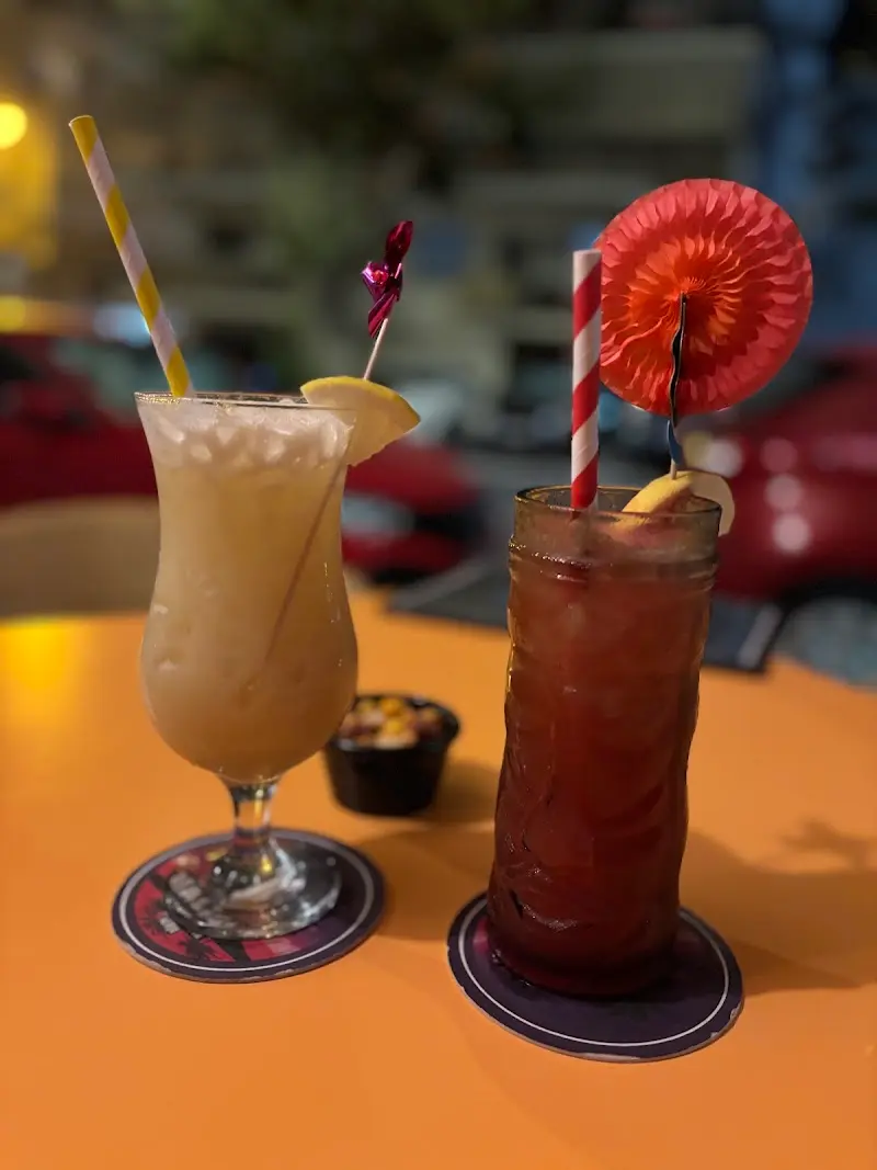 Cóctel cremoso con limón y otro rojo con sombrilla de papel sobre una mesa naranja