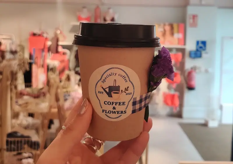 Vaso de café para llevar con el sello de la cafetería y una flor morada