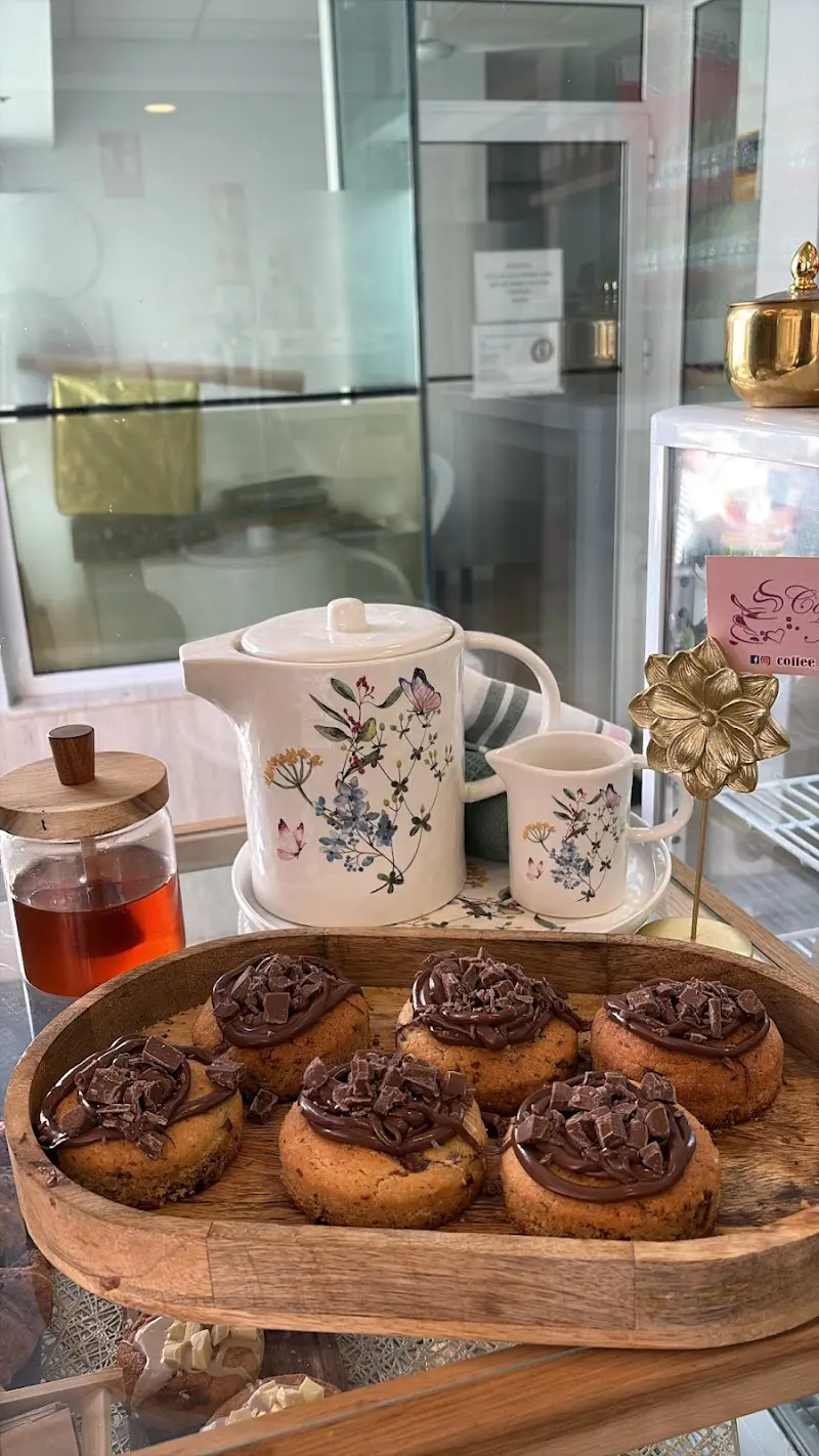 Galletas gruesas cubiertas de chocolate en bandeja de madera, junto a una tetera de flores