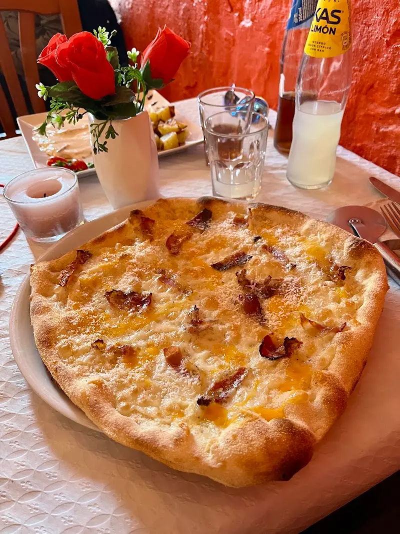 Pizza blanca con queso, huevo y beicon junto a un jarrón de rosas rojas