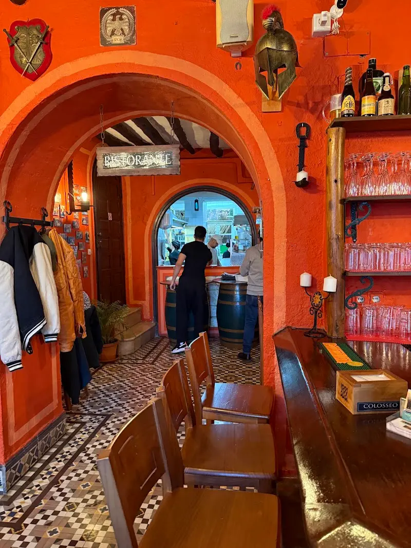 Barra y arcos de paredes naranjas con casco romano, escudos y cartel de Ristorante