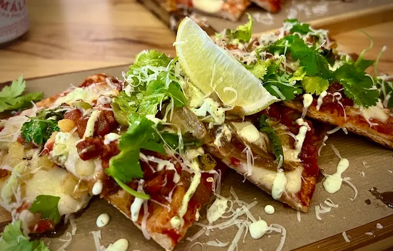 Porciones de pizza con salsa, queso rallado, cilantro y una rodaja de lima