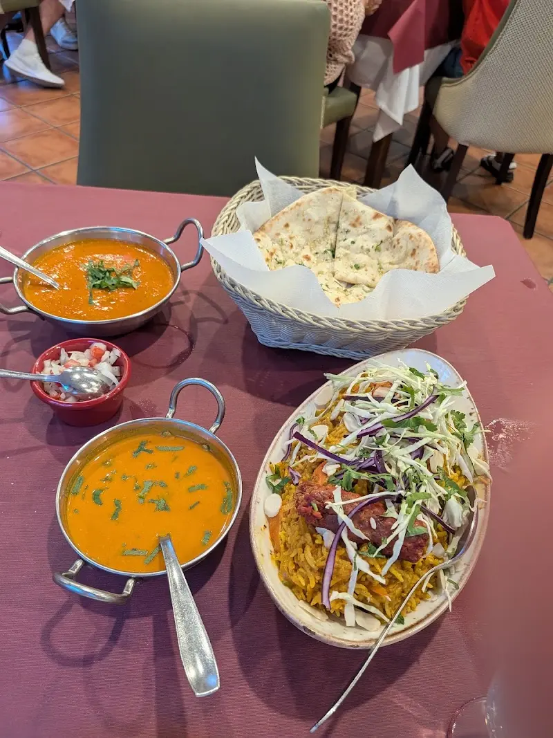 Dos currys en cazos metálicos, biryani con ensalada de col y cesta de pan naan