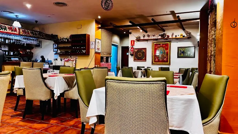 Comedor de Curry House con mesas de mantel blanco, sillas verdes y cuadros indios
