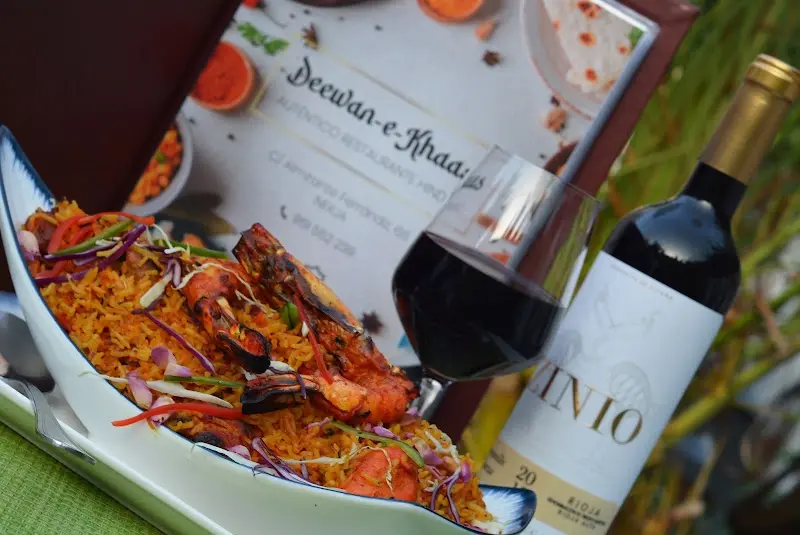 Biryani con langostinos a la brasa servido junto a la carta y una copa de vino tinto