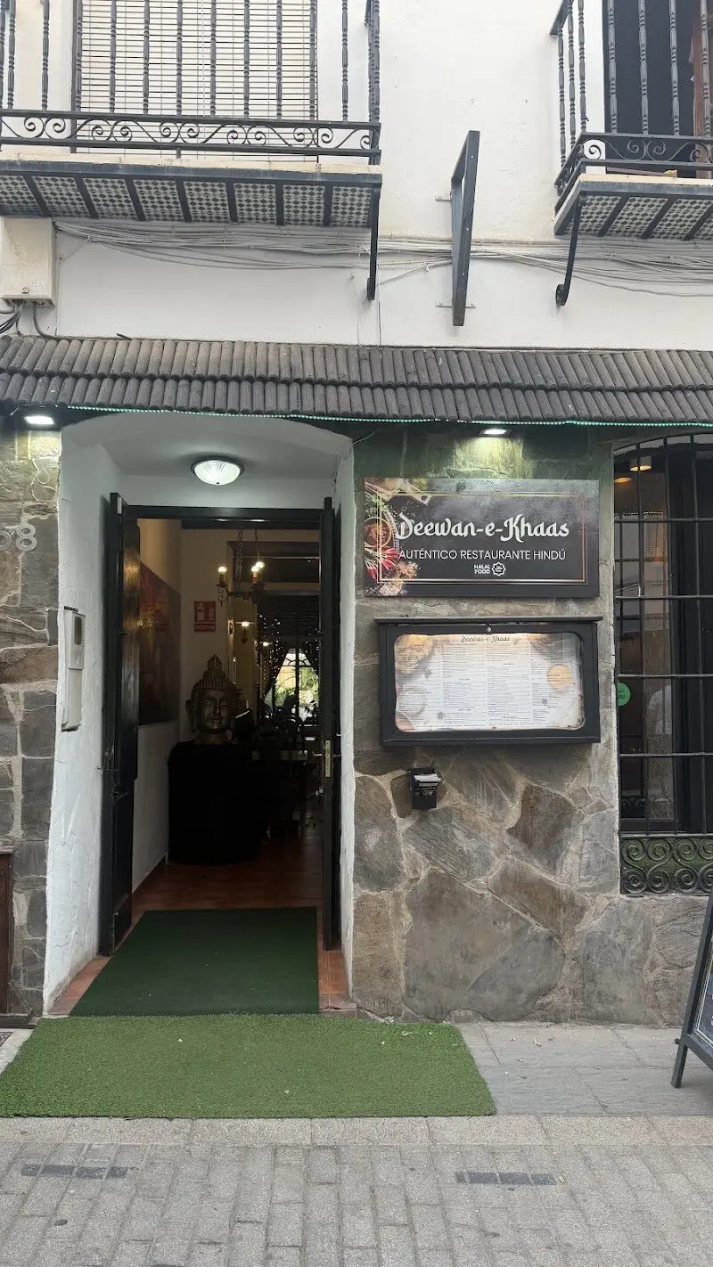 Entrada con letrero de auténtico restaurante hindú, carta expuesta y busto de Buda