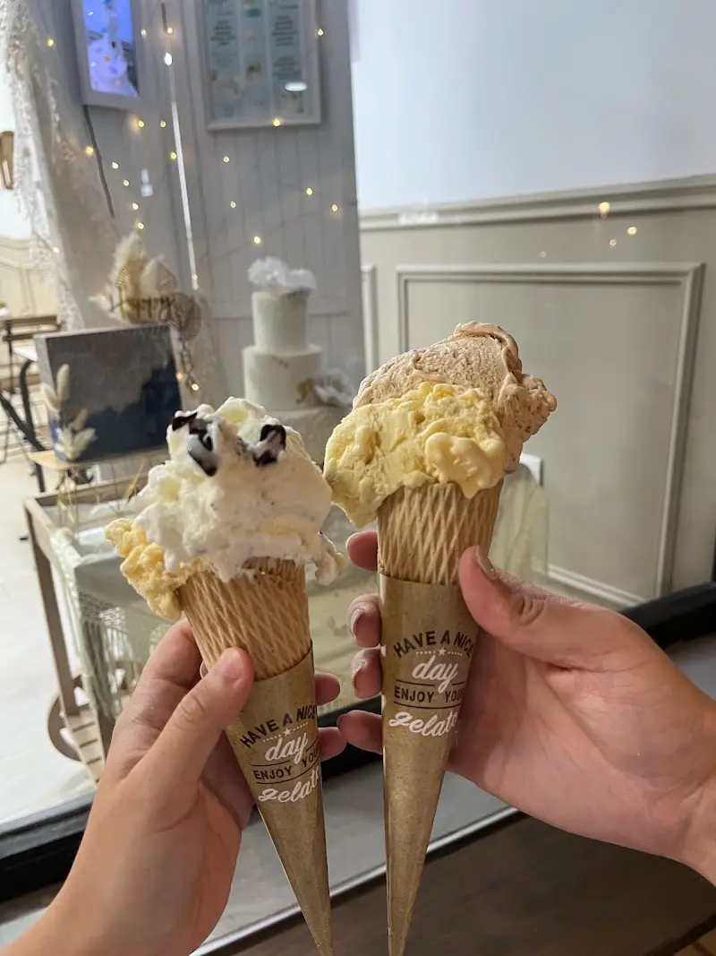 Dos cucuruchos de helado artesanal sostenidos frente a la vitrina con tartas de boda