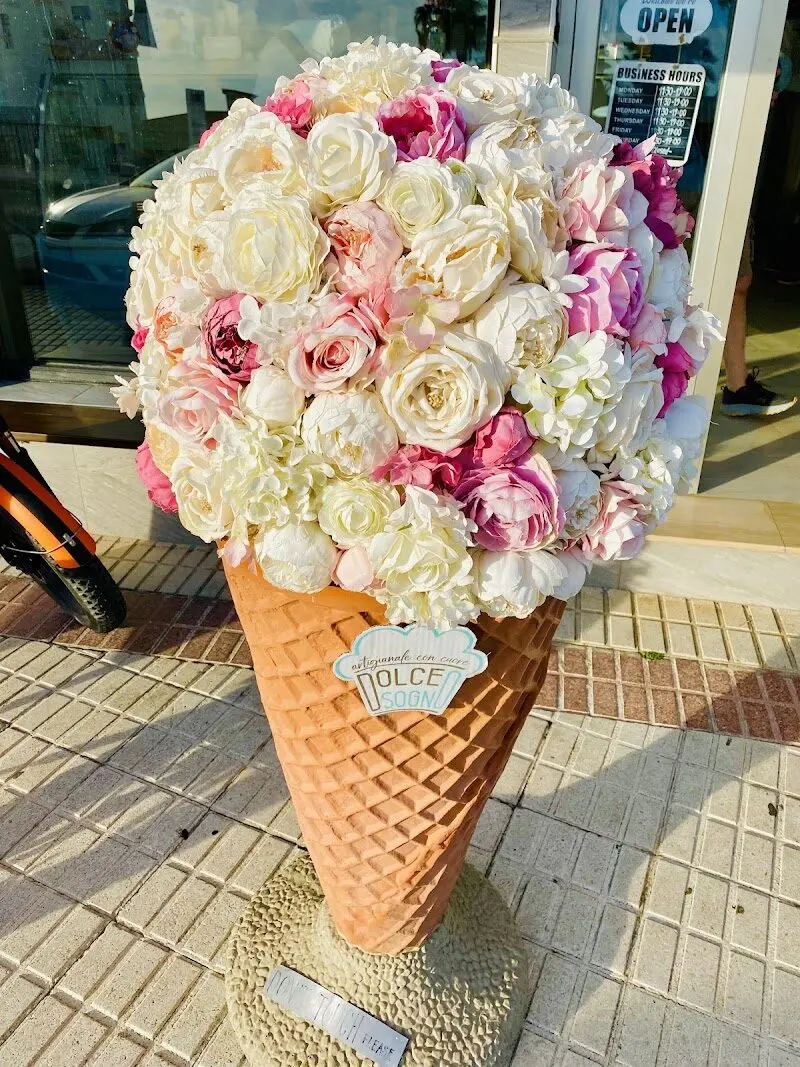 Cucurucho gigante decorativo con rosas blancas y rosas junto a la puerta de la heladería