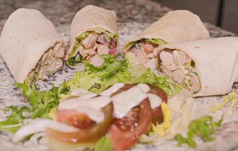 Wraps de pollo con lechuga y tomate cortados por la mitad, con ensalada y salsa
