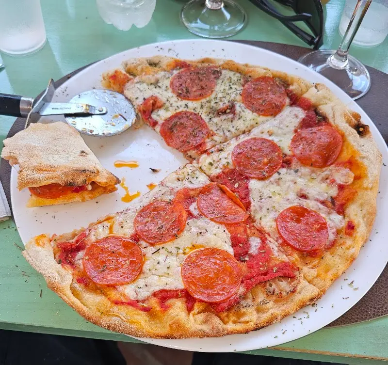 Pizza de pepperoni en porciones con cortapizzas, en una mesa de Eat Italy