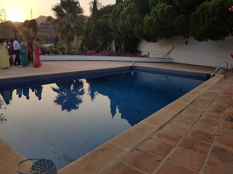 Piscina al atardecer con invitados de una celebración junto al borde y reflejos de palmeras