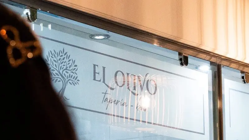 Rótulo con el olivo y el nombre de la taperia en la cristalera, de noche