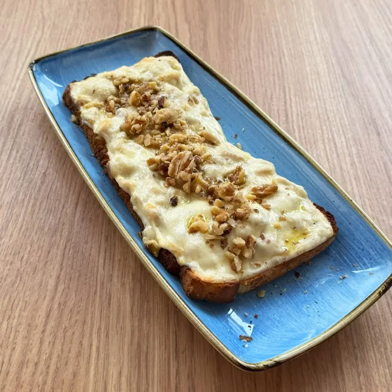 Tostada gratinada con queso fundido y nueces picadas en una fuente azul