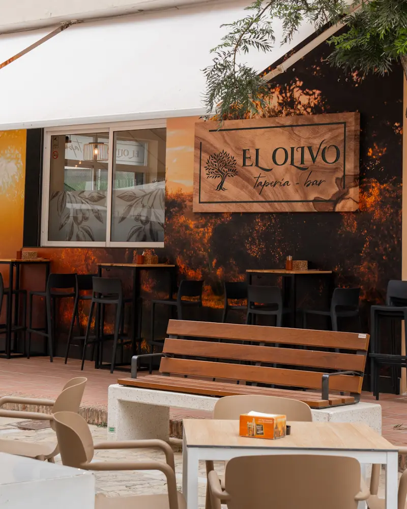 Terraza con mesas altas bajo el letrero de madera de El Olivo, taperia y bar