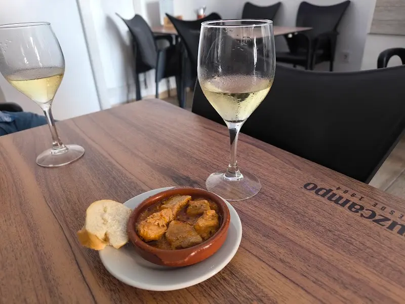 Tapa de carne en salsa en cazuelita de barro con pan y dos copas de vino blanco