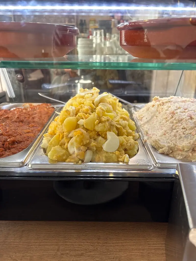 Ensalada de patata con huevo cocido entre otras bandejas de tapas en la vitrina