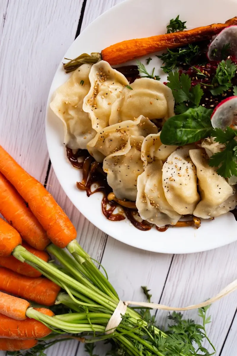 Empanadillas al vapor con sésamo, zanahoria asada, rabanitos y hojas verdes en un plato blanco