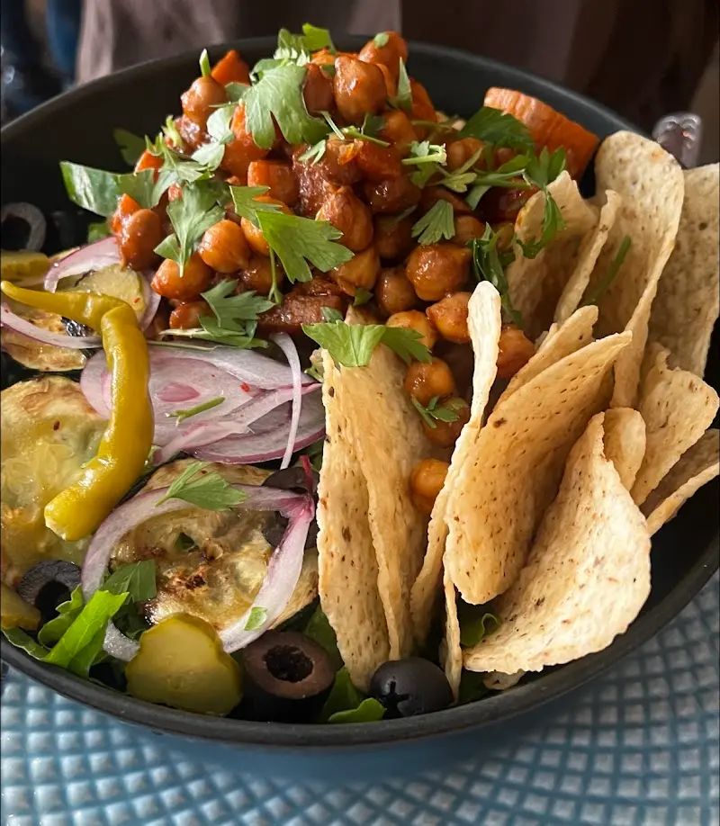 Bol vegano de garbanzos guisados con totopos, calabacín, cebolla morada, aceitunas y piparras