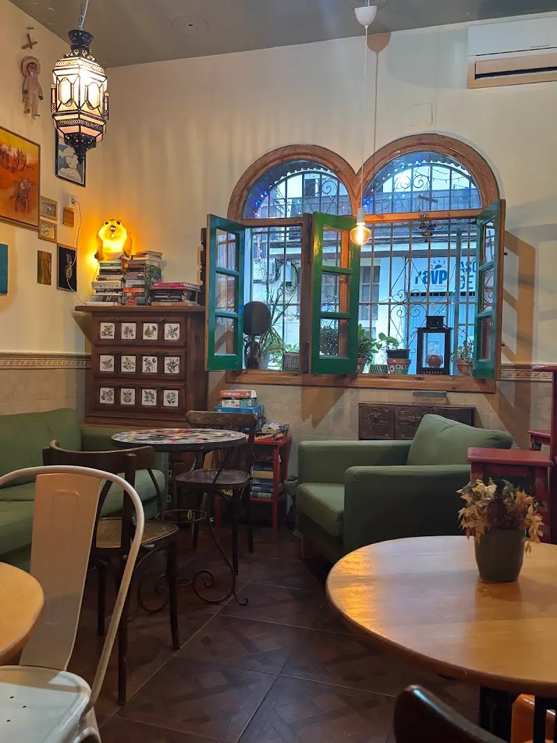 Rincón interior con sofás verdes, ventanas de arco con rejas, lámpara árabe y estante de libros