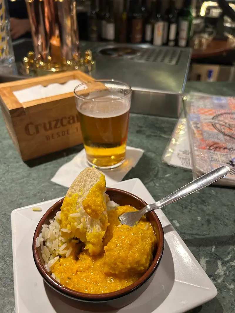 Tapa de guiso con salsa amarilla y arroz en cuenco de barro, con una caña en la barra