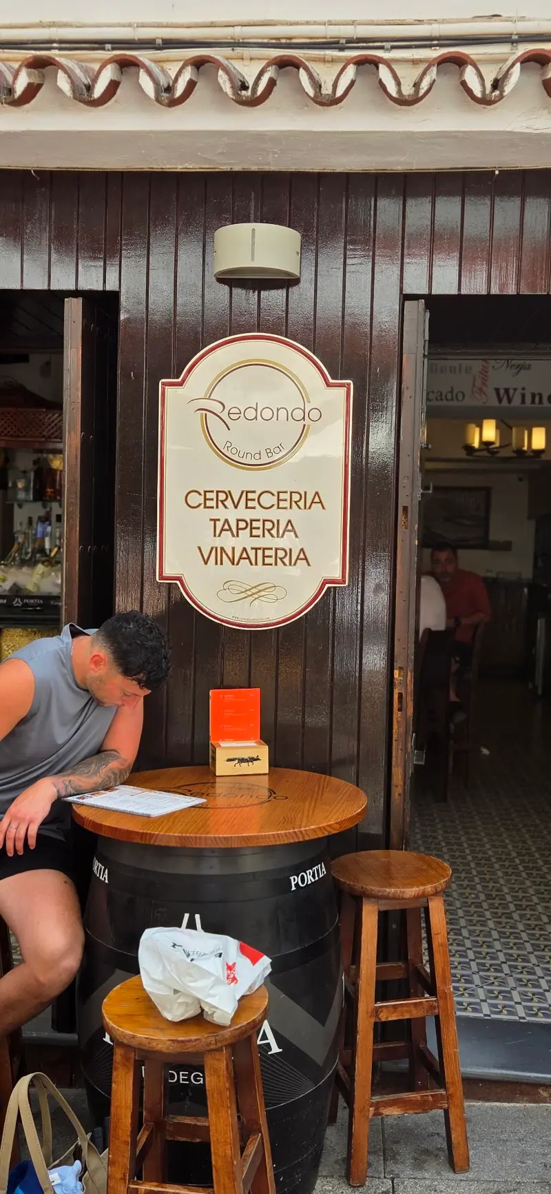 Entrada de Fish Redondo con su cartel de cervecería, tapería y vinatería y una mesa de barril