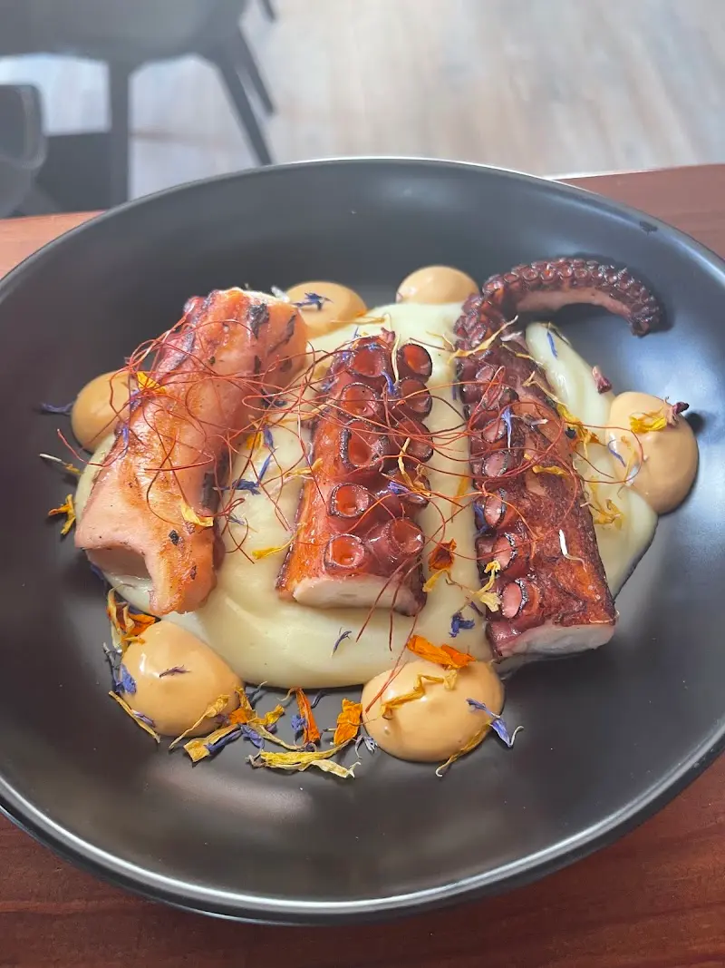 Pulpo a la brasa sobre puré de patata con salsa, hilos de guindilla y pétalos de flores