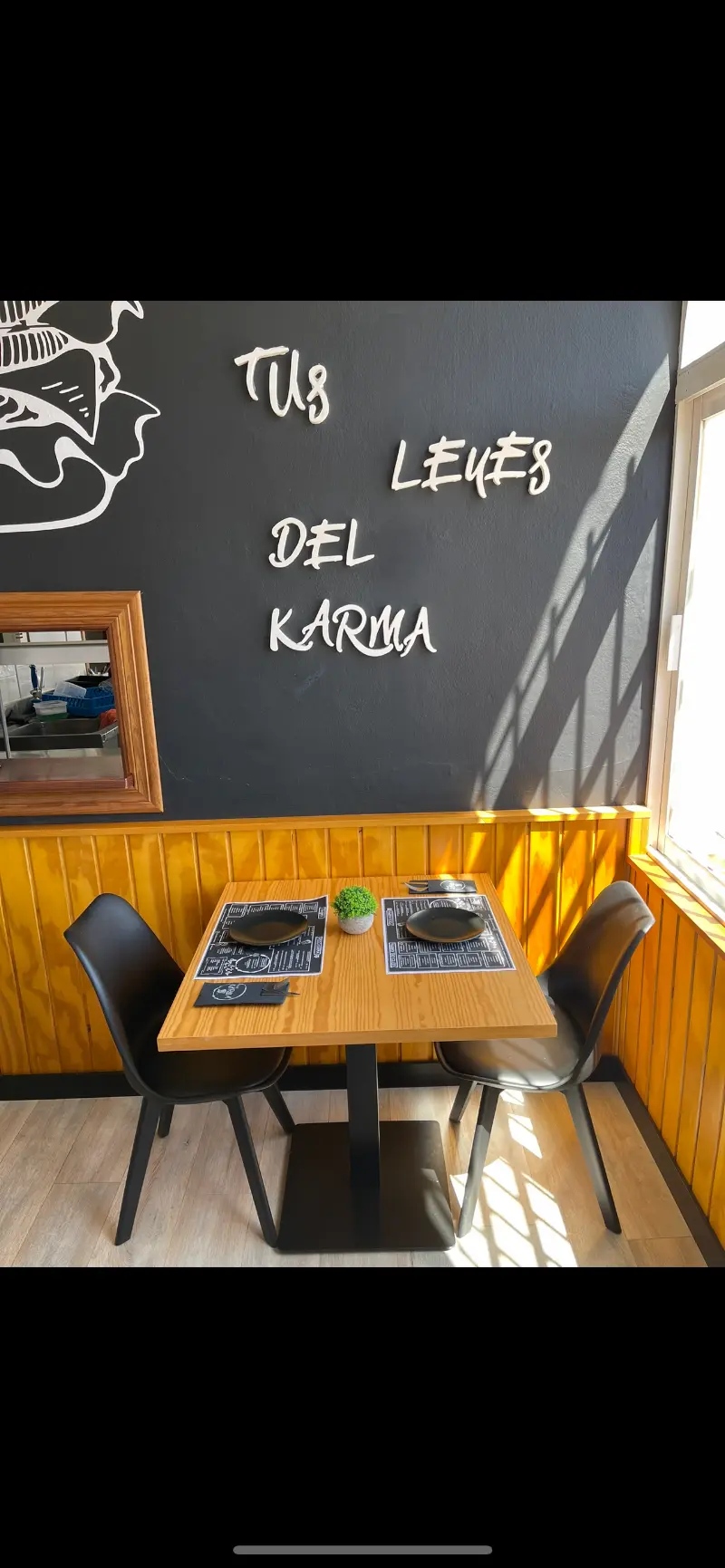 Mesa para dos bajo la pared pizarra con el lema «Tus leyes del karma» en Food Karma Gastro