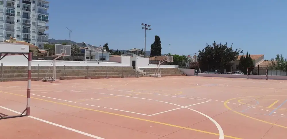 Pista polideportiva al aire libre con canastas, porterías y gradas en el Polideportivo Municipal de Nerja