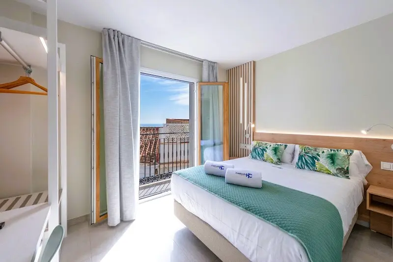 Habitación doble con cojines de hojas tropicales, colcha verde y balcón con vistas al mar