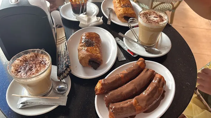 Capuchinos, napolitanas de chocolate y churros bañados en chocolate en una mesa