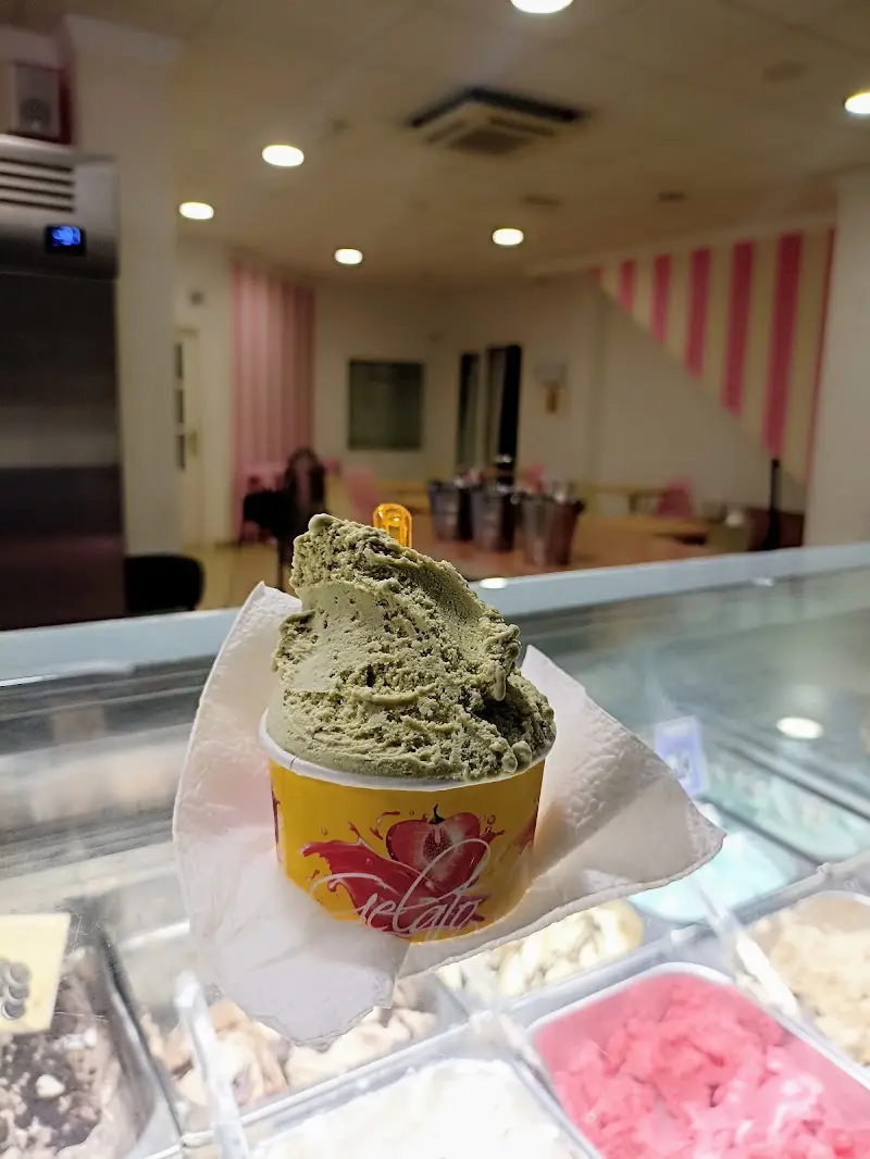 Tarrina de helado verde sostenida sobre la vitrina, con el salón rosa y blanco detrás