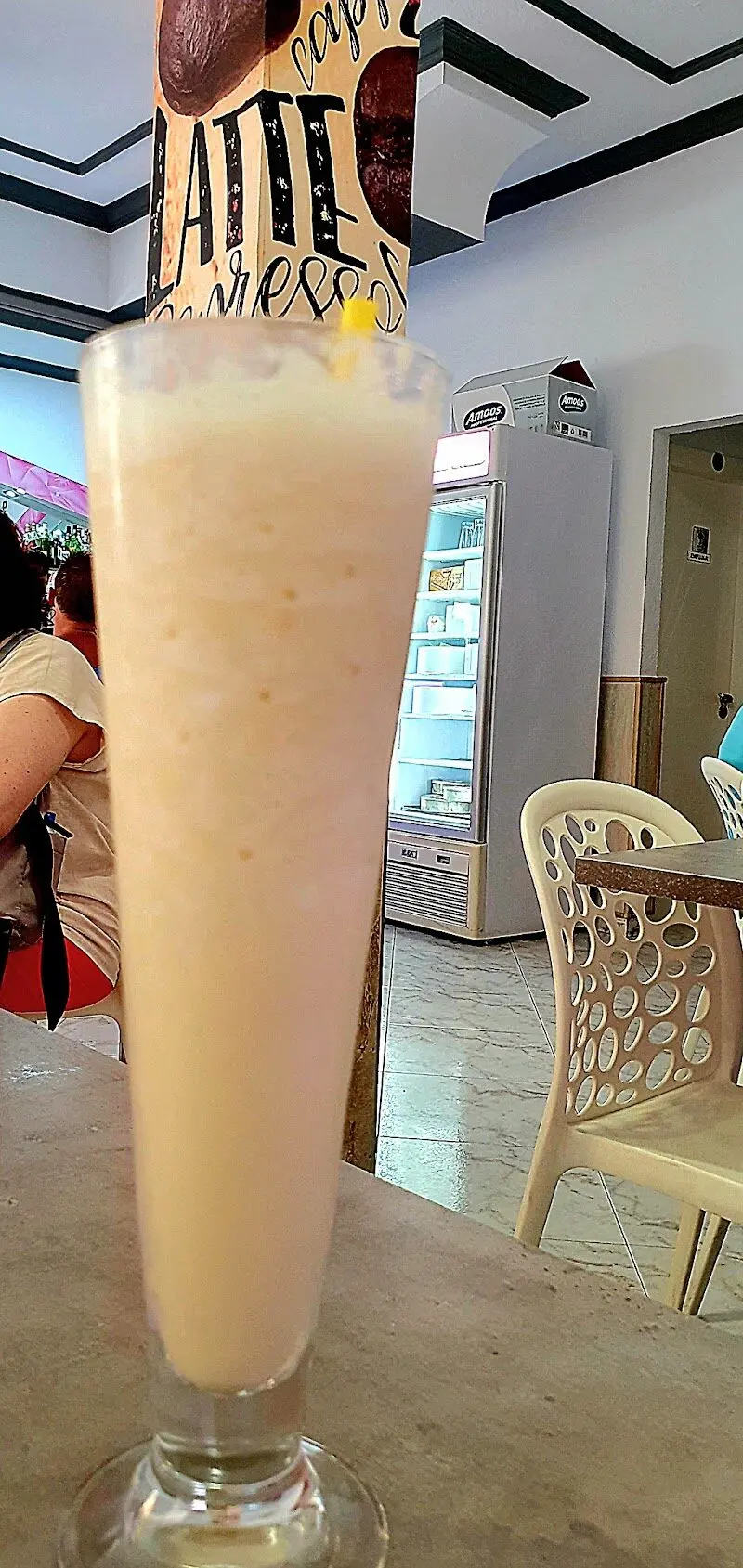 Batido en copa alta sobre una mesa, con la nevera de helados al fondo