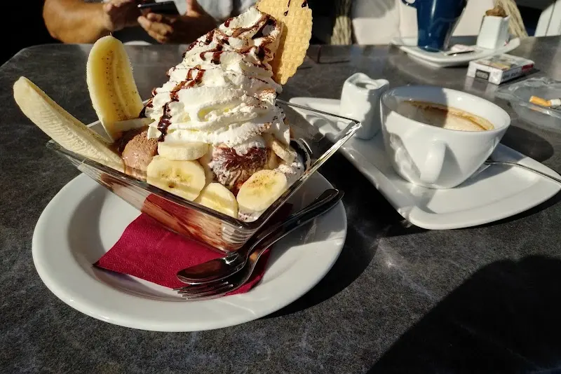Copa de helado con plátano, nata, sirope de chocolate y barquillo junto a un café